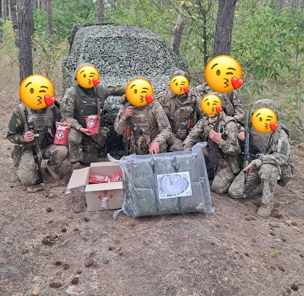 Ukrainian soldiers standing beside camouflage netting in a forest.